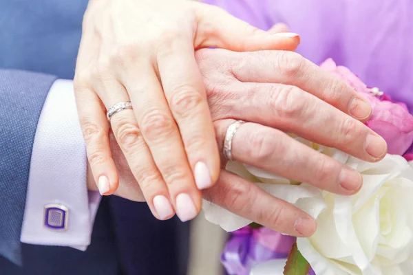 Menyasszony és a vőlegény kezét a jegygyűrű, menyasszonyi csokor virágot a háttérrel — Stock Fotó