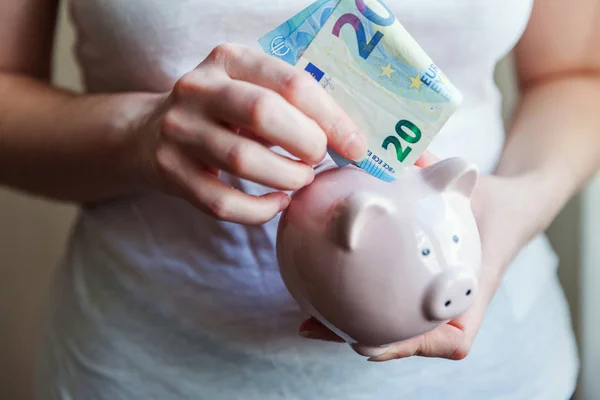 Wanita tangan memegang piggy bank merah muda dan menempatkan uang Euro — Stok Foto