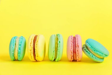 Fransız tatlı kurabiye. Çok az yiyecek ekmek kavramı. Pembe mavi sarı yeşil macaron Sarı zemin üzerine