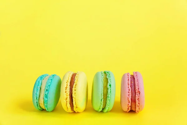 French sweet cookie. Minimal food bakery concept. Pink blue yellow green macaron on yellow background