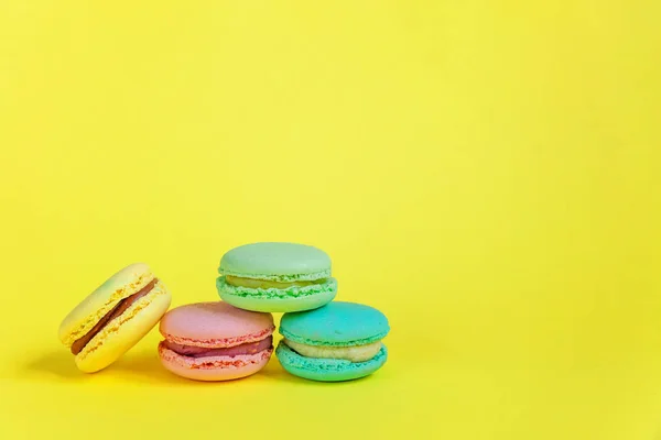 French sweet cookie. Minimal food bakery concept. Pink blue yellow green macaron on yellow background