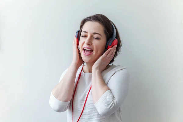 Mujer morena joven energética escuchando música en auriculares y cantando aislada sobre fondo blanco — Foto de Stock