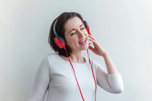 Energie junge brünette Frau hört Musik in Kopfhörern und singt isoliert auf weißem Hintergrund — Stockfoto