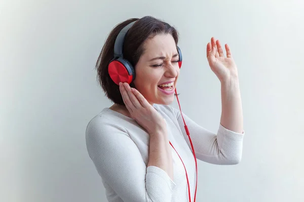 Mujer morena joven energética escuchando música en auriculares y cantando aislada sobre fondo blanco — Foto de Stock