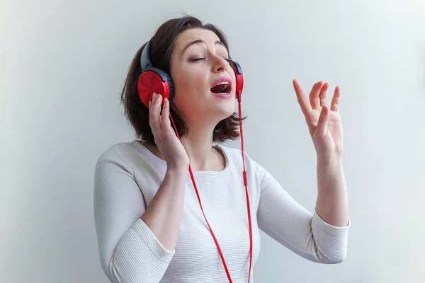 Mujer morena joven energética escuchando música en auriculares y cantando aislada sobre fondo blanco — Foto de Stock