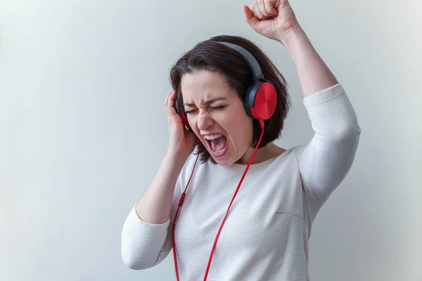 Energie junge brünette Frau hört Musik in Kopfhörern und singt isoliert auf weißem Hintergrund — Stockfoto