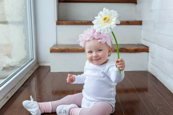 Bambina che indossa ghirlanda di primavera sito sul pavimento in luminoso soggiorno vicino alla finestra e giocare con i fiori gerbera — Foto Stock