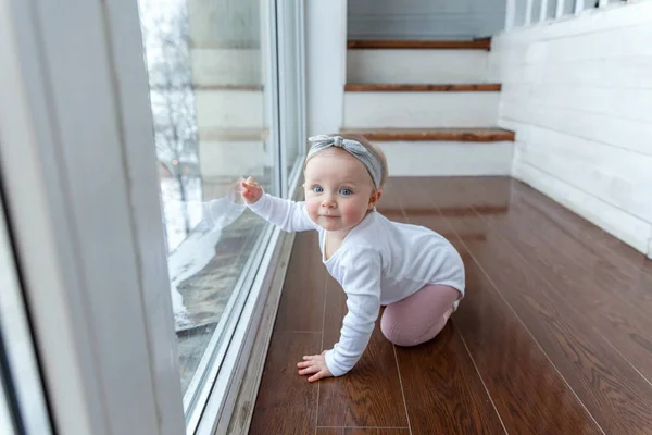 Liten flicka med krypande ett år gamla placering på golv i ljusa lätta vardagsrummet nära fönster ler och skrattar — Stockfoto