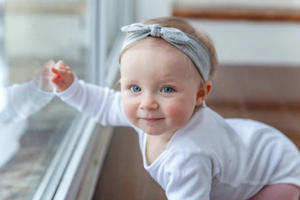 Little crawling baby girl one year old siting on floor in bright light living room near window smiling and laughing — Stock Photo, Image
