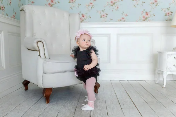 Parlak ışık oturma odasında gülümseyen ve gülüyor sandalyede yakın ayakta küçük bebek kız — Stok fotoğraf