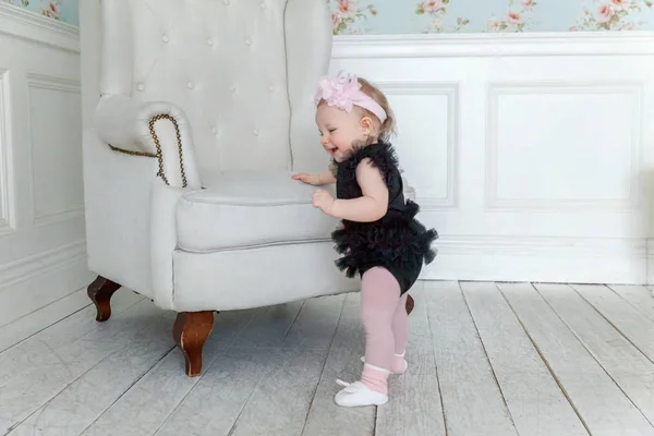 Kleines Mädchen steht neben Stuhl im hellen Wohnzimmer und lächelt und lacht — Stockfoto