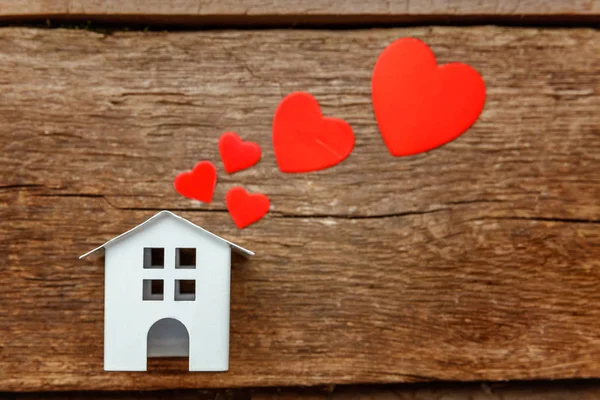 Миниатюрный белый домик с красными сердцами на деревянном фоне — стоковое фото