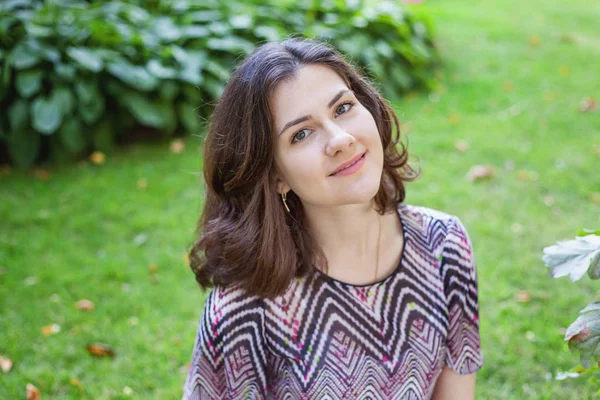 Menina morena bonita jovem com cabelos castanhos longos sorrindo no parque ou jardim fundo. Menina feliz relaxante ao ar livre — Fotografia de Stock