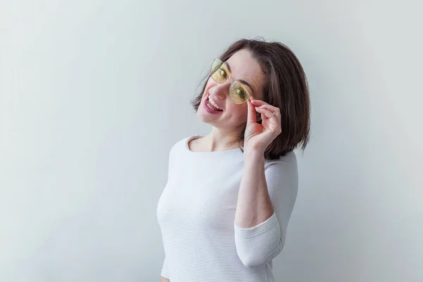 Simple studio portrait of hipster fashion smiling short-haired brunette girl in trendy yelow sunglasses isolated on white background