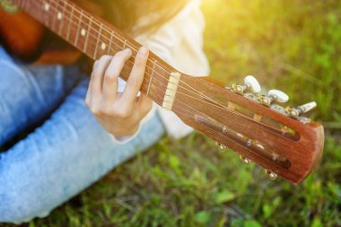 Park veya bahçe arka planda akustik gitar çalan kadın ellerinin yakın çekim. Genç kız şarkı çalmayı öğrenme ve müzik yazma