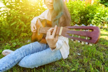 Park veya bahçe arka planda akustik gitar çalan kadın ellerinin yakın çekim. Genç kız şarkı çalmayı öğrenme ve müzik yazma