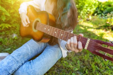 Park veya bahçe arka planda akustik gitar çalan kadın ellerinin yakın çekim. Genç kız şarkı çalmayı öğrenme ve müzik yazma