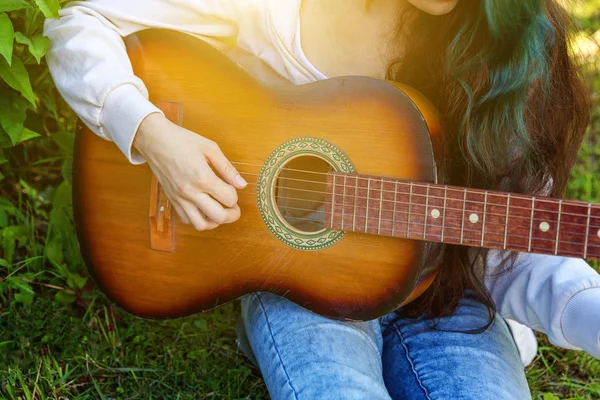 在公园或花园背景上演奏原声吉他的女性手的特写镜头。青少年女孩学习播放歌曲和写音乐 — 图库照片