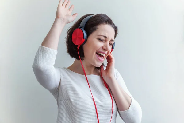 Mujer morena joven energética escuchando música en auriculares y cantando aislada sobre fondo blanco — Foto de Stock