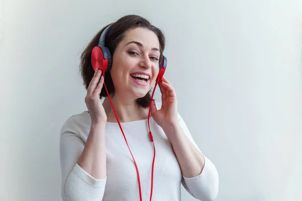 Mujer morena joven energética escuchando música en auriculares y cantando aislada sobre fondo blanco — Foto de Stock