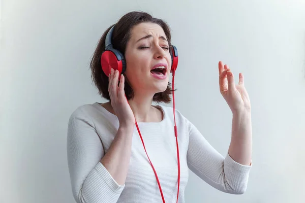 Mujer morena joven energética escuchando música en auriculares y cantando aislada sobre fondo blanco — Foto de Stock