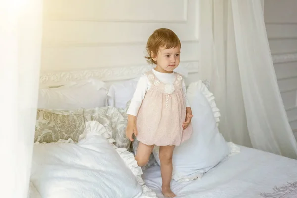 Söt liten flicka som hoppar på vit säng — Stockfoto