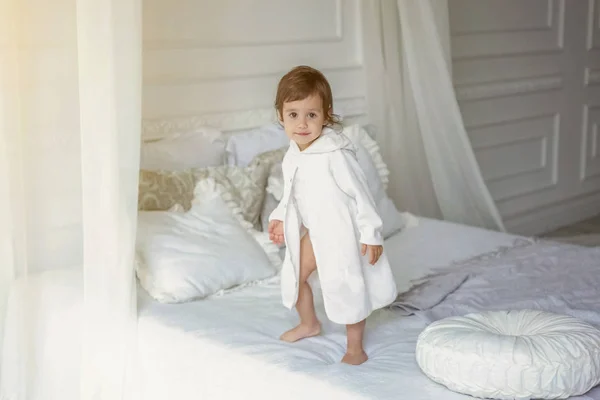 Cute little girl jumping on white bed — Stock Photo, Image