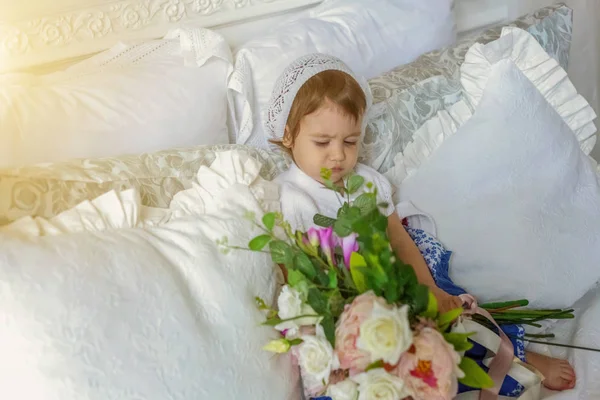 Petite fille mignonne jouant avec bouquet de fleurs sur lit blanc — Photo