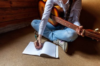 Genç hippi kadın yerde oturuyor ve evde gitar çalıyor.