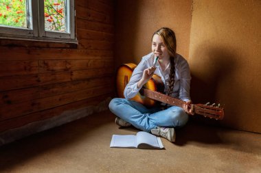 Genç hippi kadın yerde oturuyor ve evde gitar çalıyor.