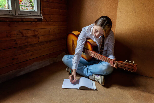 Young hipster woman sitting on floor and playing guitar at home