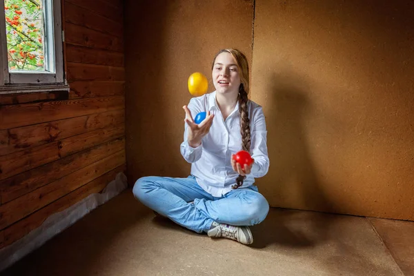 Young hipster woman sitting on floor and juggling colored balls at home — 스톡 사진