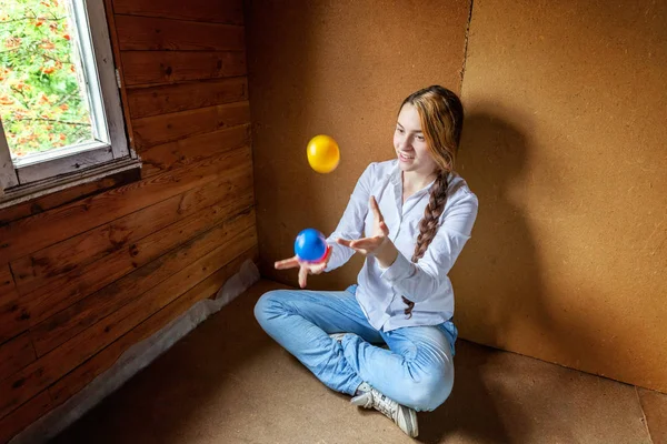 Ung hipster kvinna sitter på golvet och jonglera färgade bollar hemma — Stockfoto