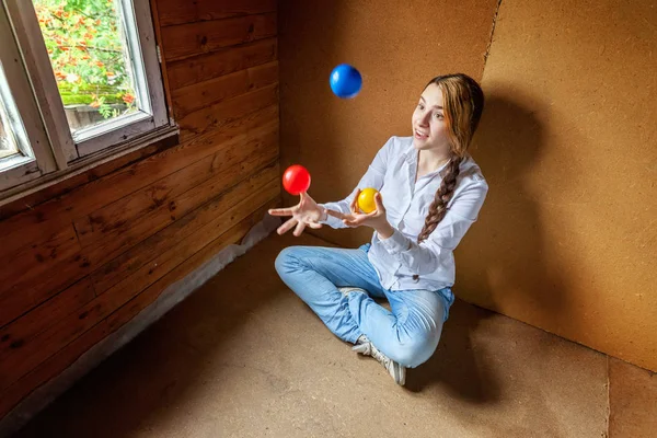Ung hipster kvinna sitter på golvet och jonglera färgade bollar hemma — Stockfoto
