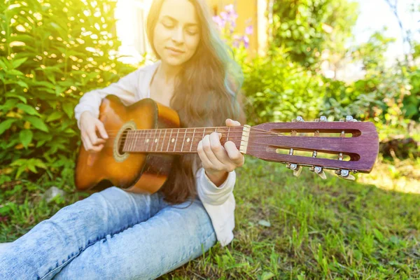 Closeup of woman hands playing acoustic guitar on park or garden background. Teen girl learning to play song and writing music — Stock Photo, Image