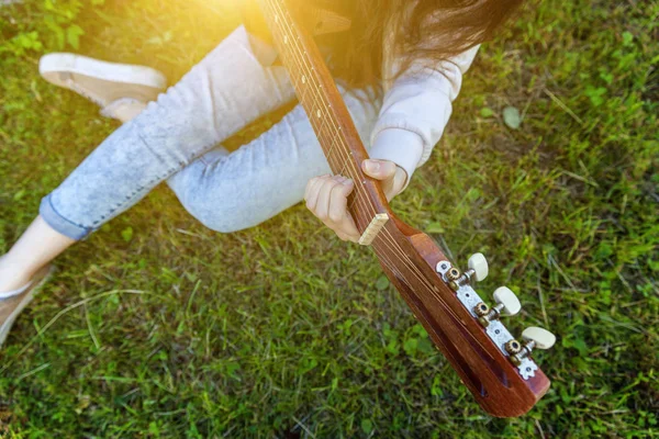 在公园或花园背景上演奏原声吉他的女性手的特写镜头。青少年女孩学习播放歌曲和写音乐 — 图库照片