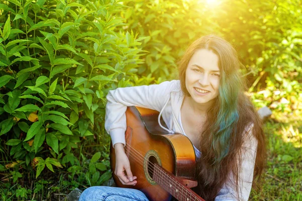 Jonge hipster vrouw zittend in gras en het spelen van gitaar op Park of tuin achtergrond. Tiener meisje leert liedjes te spelen en muziek te schrijven — Stockfoto