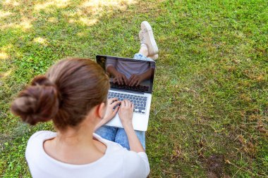 Dizüstü pc bilgisayar üzerinde çalışan Şehir Parkı yeşil çim Çimenlikte oturan genç kadın. Serbest iş kavramı
