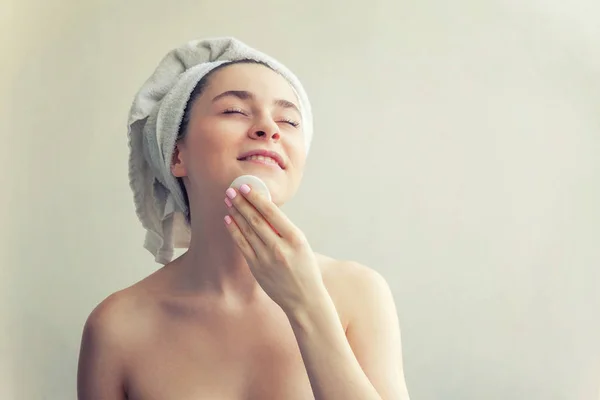 Lachende vrouw in handdoek op hoofd met zachte gezonde huid verwijderen make-up met wattenschijfje geïsoleerd op witte achtergrond — Stockfoto