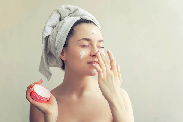 Retrato de beleza de mulher em toalha na cabeça com máscara nutritiva branca ou creme no rosto, fundo branco isolado — Fotografia de Stock