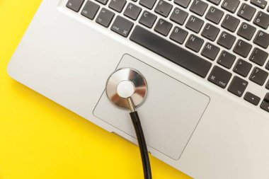 Stetoskop klavye dizüstü bilgisayar sarı arka plan üzerinde izole. Modern tıbbi Bilgi teknolojisi ve sofware gelişmeler kavramı. Bilgisayar ve gadget tanılama ve onarım