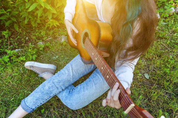 Closeup of woman hands playing acoustic guitar on park or garden background. Teen girl learning to play song and writing music — Stock Photo, Image