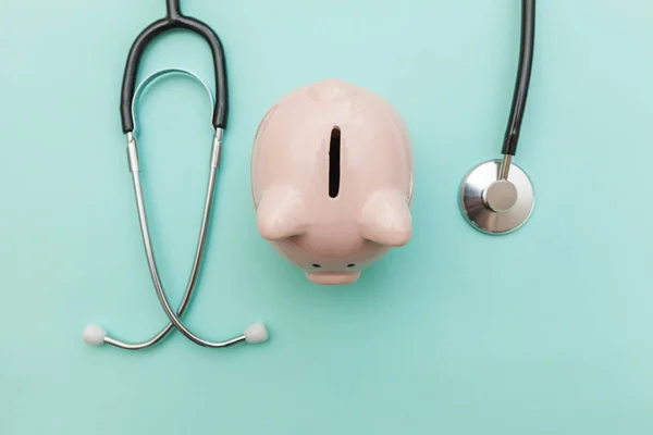 Geneeskunde arts apparatuur stethoscoop of phonendoscoop en Piggy Bank geïsoleerd op trendy pastel blauwe achtergrond — Stockfoto