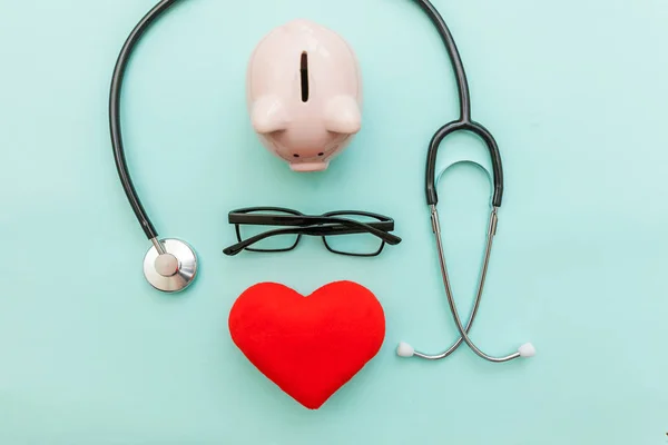 Equipamento médico medicina estetoscópio ou fonendoscópio óculos de banco piggy e coração vermelho isolado no moderno fundo azul pastel — Fotografia de Stock