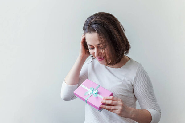 Young positive woman holding small pink gift box isolated on white background. Preparation for holiday. Girl looking happy and excited