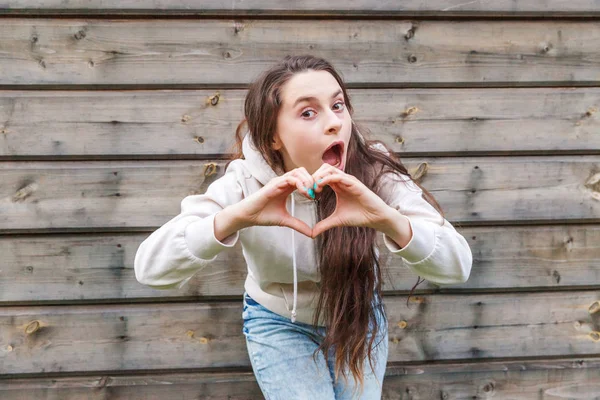 Sevgi, kalp şekli, barış. Güzellik portre genç mutlu pozitif kadın ahşap duvar arka plan üzerinde elleri ile kalp işareti gösteren