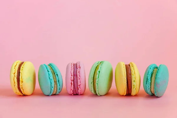 French sweet cookie. Minimal food bakery concept. Pink blue yellow green macaron on pink background