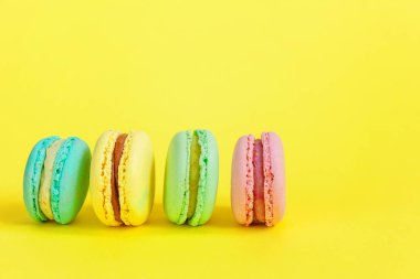 Fransız tatlı kurabiye. Çok az yiyecek ekmek kavramı. Pembe mavi sarı yeşil macaron Sarı zemin üzerine