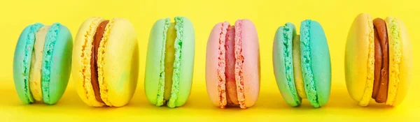 French sweet cookie. Minimal food bakery concept. Pink blue yellow green macaron on yellow background