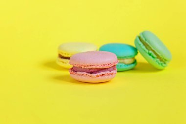 Fransız tatlı kurabiye. Çok az yiyecek ekmek kavramı. Pembe mavi sarı yeşil macaron Sarı zemin üzerine